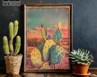 Könnte beinhalten: Ein gerahmter Kunstdruck einer Wüstenlandschaft mit einem großen Kaktus mit gelben und blauen Polstern, einer rosa Blüte und einem Sonnenuntergangshimmel. Der Druck wird auf einer Holzoberfläche mit einem Topfkaktus und einer Sukkulente auf beiden Seiten präsentiert. Das Logo von Wiley & Co. Mercantile ist sichtbar.