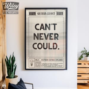 Pu&ograve; includere: Una stampa incorniciata in nero con sfondo bianco e testo nero che recita "CAN'T NEVER COULD." Il testo &egrave; in un font in stile giornale vintage. Sotto il testo c'&egrave; una sezione pi&ugrave; piccola con il titolo "VOL.II SOUTHERN SAYINGS EXPLAINED" e una definizione della frase.