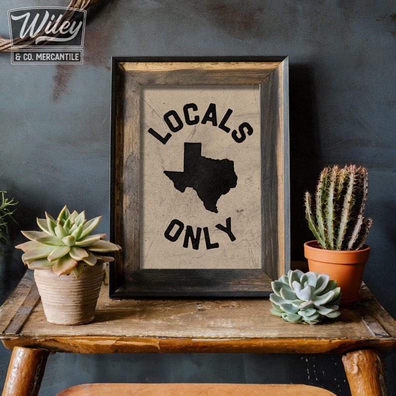 May include: A framed print with a distressed, beige background featuring a black silhouette of the state of Texas with the text "Locals Only" in a black, distressed font.