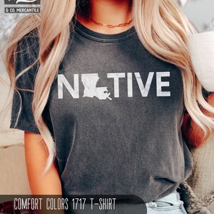 May include: Dark gray Comfort Colors 1717 t-shirt with the word "NATIVE" in white block letters, featuring the outline of Louisiana. The shirt is pepper-colored and has a vintage look. The Wiley & Co. Mercantile logo is in the upper left corner.