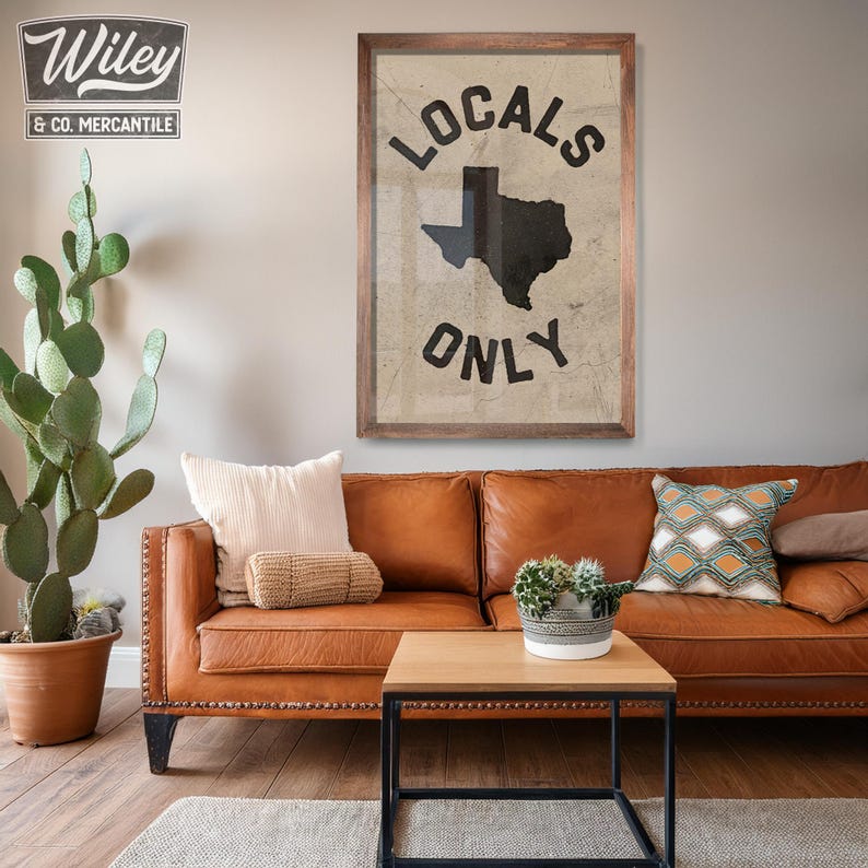 May include: A brown leather sofa with a framed print that says "Locals Only" and features a black silhouette of the state of Texas. The sofa is decorated with throw pillows and a potted plant.