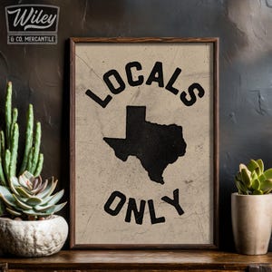 May include: A vintage-style print with a black silhouette of the state of Texas and the text "LOCALS ONLY" in a bold, black font. The print is on a beige background and framed in a dark wood frame.
