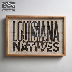 May include: A framed print with the text "LOUISIANA NATIVES" in black lettering on a beige background.