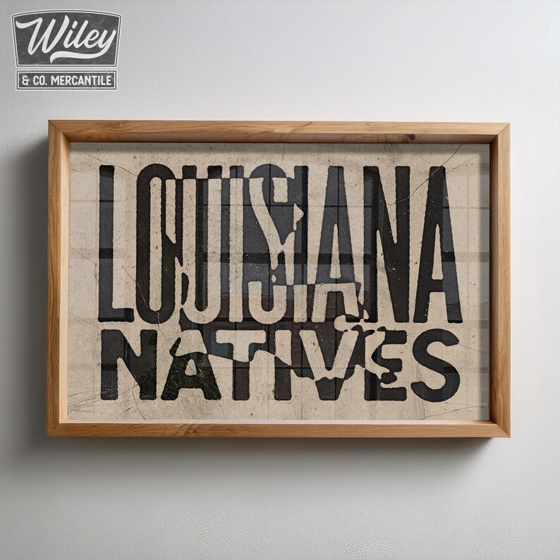 May include: A framed print with the text "LOUISIANA NATIVES" in black lettering on a beige background.
