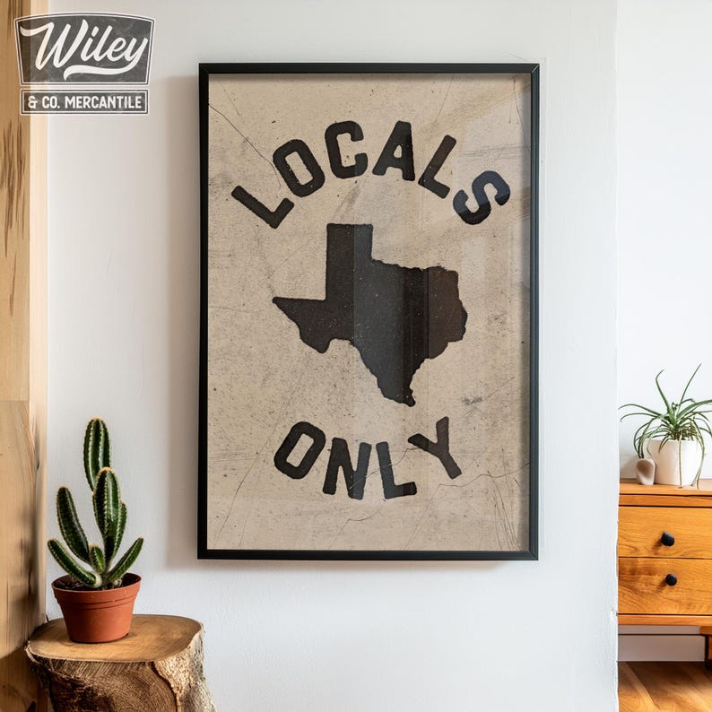 May include: A black framed print with a vintage aesthetic. The print features a black silhouette of the state of Texas with the text "Locals Only" in a bold, blocky font.