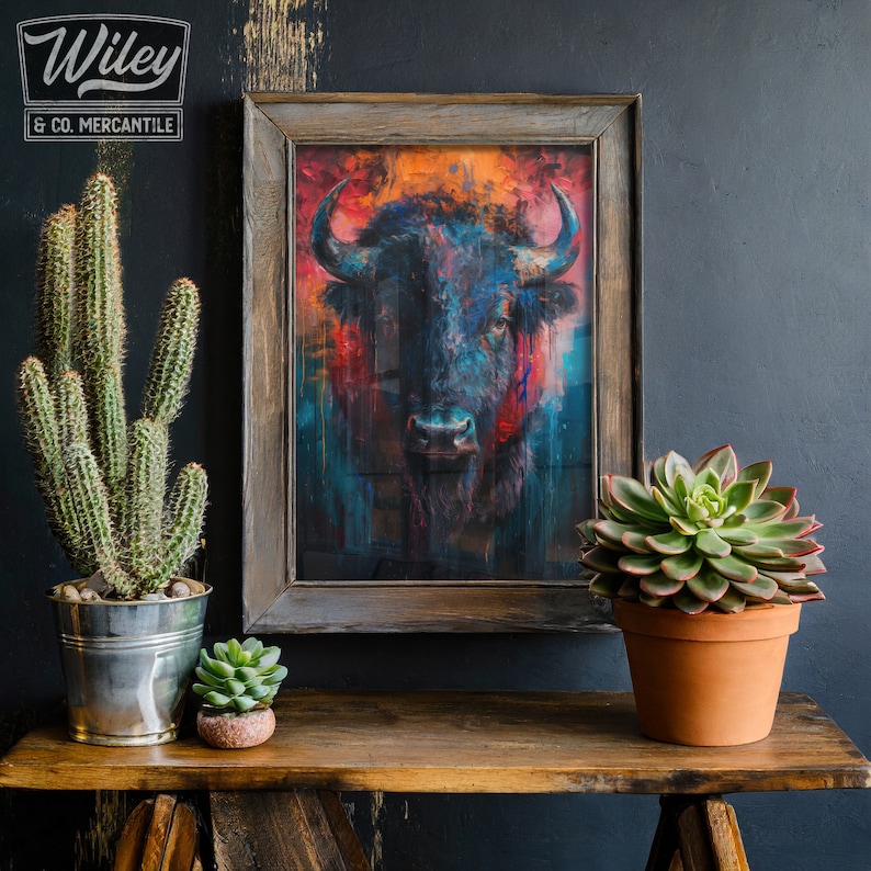May include: A framed art print of a bison with a colorful, abstract design. The artwork features a dark bison with blue, red, and orange hues. The print is displayed on a wooden shelf with potted plants, including a cactus and a succulent. The Wiley & Co. Mercantile logo is in the top left corner.