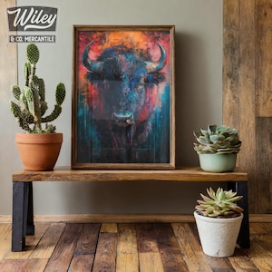 May include: A framed art print featuring a colorful, abstract depiction of a bison. The artwork uses vibrant blues, reds, and oranges. The print is displayed on a wooden bench alongside potted plants, including a cactus and succulents. The Wiley & Co. Mercantile logo is visible.