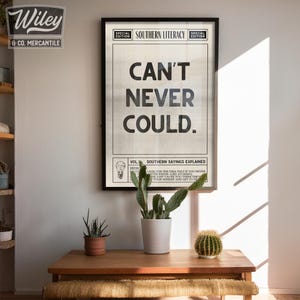 Pu&ograve; includere: Una stampa in bianco e nero con il testo "CAN'T NEVER COULD." La stampa &egrave; incorniciata e appesa a un muro bianco. Il testo &egrave; in un font in stile giornale e la stampa ha un aspetto vintage. La stampa fa parte di una serie chiamata "Southern Literacy" e include il testo "Southern Sayings Explained".