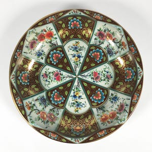 Può includere: Un vassoio rotondo in metallo con sfondo bianco e un motivo floreale colorato. Il vassoio ha un bordo dorato e un design floreale marrone e verde.