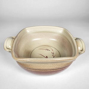 Puede incluir: Un cuenco cuadrado de cerámica con dos asas. El cuenco tiene un exterior beige y marrón moteado con una banda marrón más oscura alrededor de la base. En el interior, hay un diseño pintado en marrón simple.