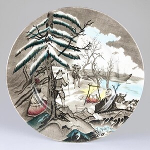 May include: A decorative plate featuring a historical scene with figures near a campfire, a ship, and a snowy landscape. The plate has a gray and white color scheme with accents of blue and red. The design depicts a winter scene with a detailed illustration.