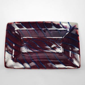 May include: A rectangular glass tray featuring a deep burgundy and dark purple base colour. The surface is decorated with diagonal, wavy stripes in shades of dark blue and metallic silver, creating a layered, glossy, and textured appearance.