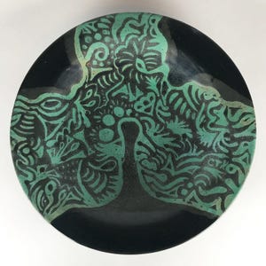 Puede incluir: Un plato de cerámica negro con un diseño abstracto verde y negro. El diseño recuerda a un árbol con ramas y hojas.