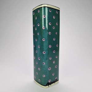 May include: A tall, rectangular ceramic vase with a teal green background and a pattern of pink circles. The vase has a cream-colored rim and base with black trim. The artist's signature is visible on the bottom.