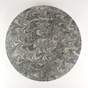 Puede incluir: Un plato redondo de mármol blanco y negro con un patrón de remolino rosa. El plato tiene un diseño ondulado.