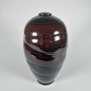 Könnte beinhalten: Eine glänzende Keramikvase in Dunkelburgunder und Schwarz. Die Vase hat einen abgerundeten Körper und einen schmalen Hals. Die Oberfläche hat ein strukturiertes, wirbelndes Muster. Die Vase eignet sich für die Inneneinrichtung.