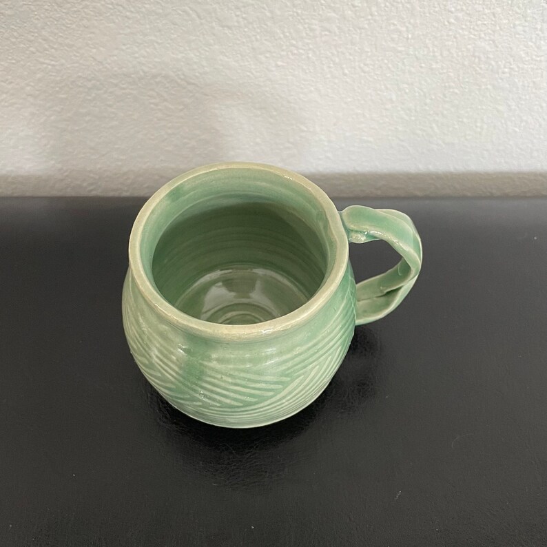 May include: A green ceramic mug with a textured, wavy design. The mug has a rounded body and a handle.