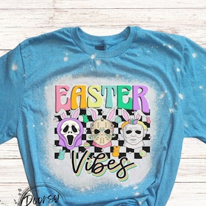 May include: A blue t-shirt with a bleached design featuring three horror movie character masks with bunny ears and the text "Easter Vibes".