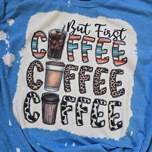 May include: A blue tie-dye t-shirt with a white graphic that says "But First Coffee" with three coffee cups in different styles.