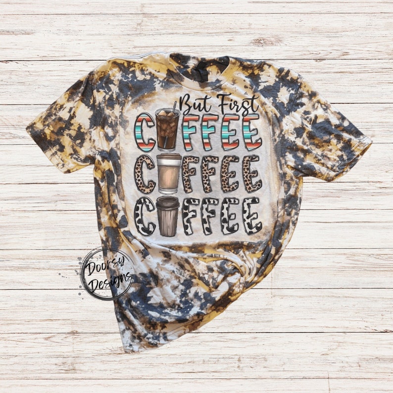 May include: A bleached tie-dye t-shirt with a brown and black pattern. The shirt features the text "But First Coffee" with three coffee cups in different styles.