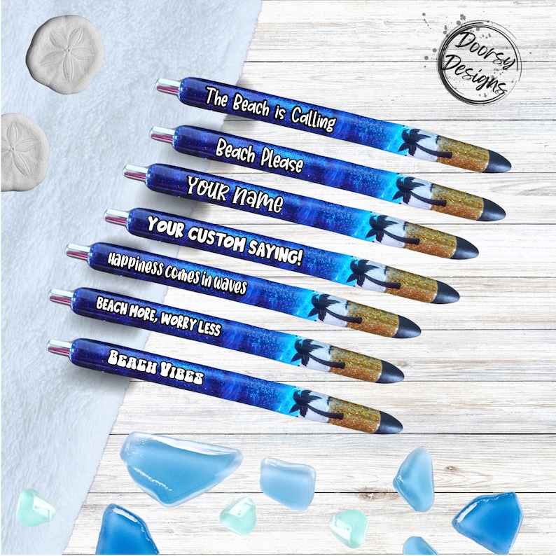 May include: Set of six blue and gold pens with beach-themed designs. The pens feature palm trees, sand, and ocean waves. The text on the pens reads: "The Beach is Calling", "Beach Please", "YOUR name", "YOUR CUSTOM SAYING!", "Happiness comes in waves", "BEACH MORE, WORRY LESS", and "BEACH VIBES".