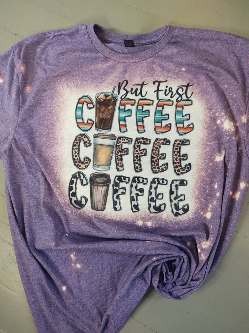 May include: Purple t-shirt with a bleached design featuring the text "But First Coffee" with three coffee cups in different styles.