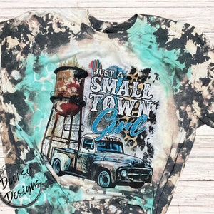 May include: A tie-dye t-shirt with a vintage truck and water tower graphic. The text on the shirt reads "Just a Small Town Girl".