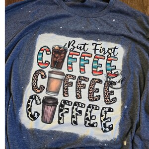 May include: A blue t-shirt with a white design that says "But First Coffee" with three coffee cups in different styles. The coffee cups are surrounded by a leopard print design.