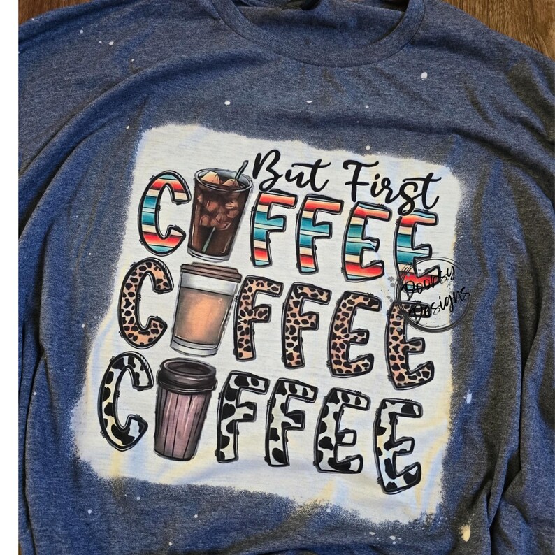 May include: A blue t-shirt with a white design that says "But First Coffee" with three coffee cups in different styles. The coffee cups are surrounded by a leopard print design.