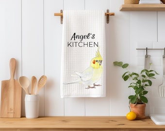 Op de afbeelding: Witte keukendoek met een gele kaketoe en de tekst "Angel's Kitchen" erop gedrukt.