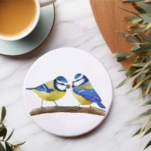 Könnte beinhalten: Zwei Blaumeisen mit gelben Brüsten sitzen auf einem Ast. Der Vogel links schaut nach rechts, während der Vogel rechts nach links schaut. Die Vögel sind in einem realistischen Stil auf einem weißen Keramikuntersetzer gemalt.