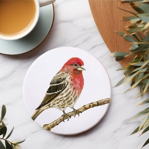 Könnte beinhalten: Ein weißer Untersetzer aus Keramik mit einer Aquarell-Illustration eines rotbrüstigen Vogels, der auf einem Ast sitzt. Der Vogel hat einen braunen und grauen Körper mit einer roten Brust und einem schwarzen Auge.