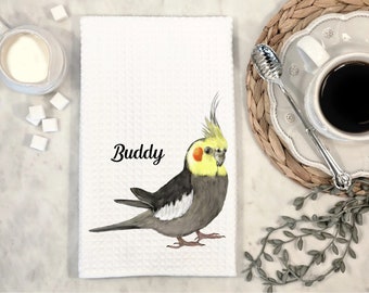 Op de afbeelding: Witte keukendoek met een illustratie van een gele en grijze kaketoe. De vogel kijkt naar rechts en heeft een gele kop en een grijs lichaam. De tekst "Buddy" is in zwart onder de vogel gedrukt.