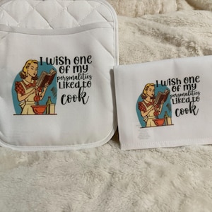 May include: White quilted oven mitt and matching kitchen towel set. Each item features a retro illustration of a woman reading a cookbook, with the text "I wish one of my personalities liked to cook."