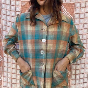 May include: A vintage plaid jacket in shades of teal, orange, and beige. The jacket features a collared neckline, large white buttons, and two front pockets. The long-sleeved jacket is buttoned up and has a relaxed fit.