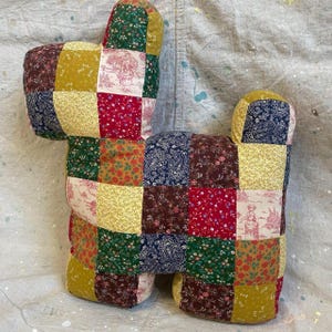 May include: A stuffed animal shaped like a dog, constructed from a patchwork of various fabric squares. The fabric features diverse patterns including floral prints, paisley designs, and toile scenes in shades of mustard yellow, red, green, and navy.