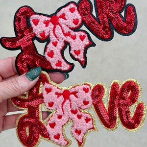 May include: Two decorative patches with the word "LOVE". One patch features red sequins with a black border and a pink bow with red hearts. The other has red sequins with a gold border and a pink bow with red hearts.