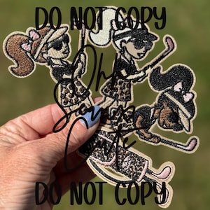 May include: Embroidered patches featuring three cartoon golfers in black outfits with leopard print skirts and sunglasses. Each golfer is holding a golf club. The patches have a tan border and the text "DO NOT COPY" is visible.
