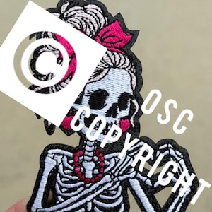 May include: Embroidered patch featuring a skeleton with a pink bow, a red beaded necklace, and a black outline. The patch has the word "COPYRIGHT" in white text. The skeleton's skull is light blue.