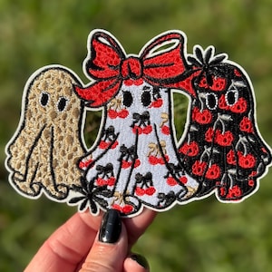May include: Three embroidered ghost patches. The first is tan with black stitching. The second is white with a red bow and cherry pattern. The third is black with a red cherry pattern. All have a white border.