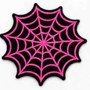 May include: A circular embroidered patch featuring a vibrant hot pink spider web design stitched onto a solid black fabric base. The web pattern radiates from the center with concentric curved lines, creating a distinct contrast against the black.