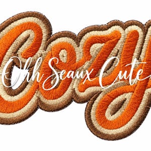 May include: An embroidered patch featuring the word COZY in bold, layered script lettering with orange, cream, and dark brown thread. Overlaid in the center is the white cursive text Ohh Seaux Cute, creating a multi-layered design.