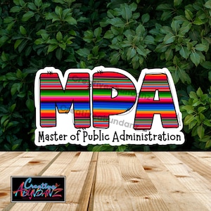 Puede incluir: Una pegatina con las letras "MPA" en rayas coloridas, con las palabras "Master of Public Administration" debajo. La pegatina tiene un borde blanco y está sobre un fondo de hojas verdes y una superficie de madera.