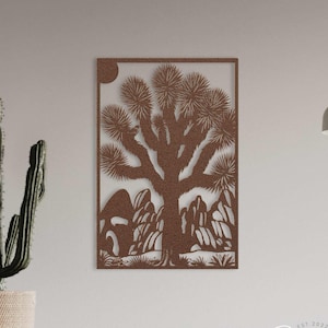 May include: Copper metal wall art featuring a Joshua tree and desert landscape design. The artwork is rectangular and hangs on a neutral wall. A cactus in a pot is to the left. The words "COPPER" are at the bottom left.