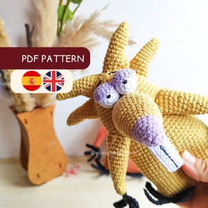 Puede incluir: Patrón de crochet para un personaje de dibujos animados amarillo con ojos y nariz morados. El patrón está disponible en español e inglés. El patrón se llama "PDF PATTERN".