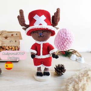 Puede incluir: Una figura amigurumi de ganchillo de un personaje que lleva un sombrero rojo con una cruz blanca, un atuendo rojo con ribetes blancos y astas marrones. La figura sostiene un algodón de azúcar rosa. El texto "Amigurumi PDF Pattern" es visible.