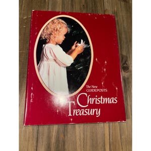May include: A red hardcover book titled "Christmas Treasury" with a picture of a young child decorating a Christmas tree. The book has the text "The New Guideposts" on the cover.