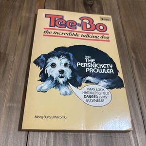 May include: A vintage children's book titled "Tee-Bo the incredible talking dog" with an illustration of a black and white dog. The book also features the text "AND THE PERSNICKETY PROWLER". The cover has a yellow background.