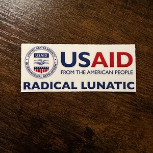 May include: A white rectangular sticker with the text "USAID" in blue and red, and the words "FROM THE AMERICAN PEOPLE" below it. The sticker also includes the text "RADICAL LUNATIC" in blue.