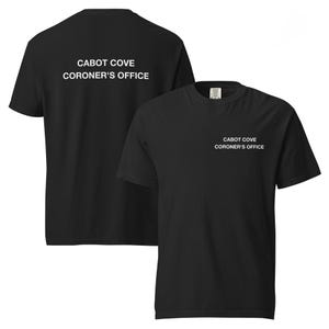 Può includere: Una t-shirt nera a maniche corte con testo bianco sul petto a sinistra e una versione più grande dello stesso testo sul retro. Il testo recita CABOT COVE CORONER'S OFFICE in un carattere sans-serif semplice e chiaro sia sul davanti che sul retro.